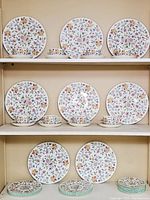 Three dinner plates displayed with matching teacups and saucers on top shelf, three on middle shelf, two dinner plates and stacks of side plates on bottom shelf