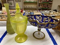 Set of three glass items on white cloth: frosted uranium yellow vase, covered uranium candy dish, and cobalt blue decorated glass candy bowl.