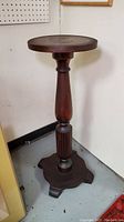 Full view of dark-finished solid wood pedestal plant stand showing turned column and shaped base