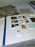 Photo showing collection of vintage postage stamps, black and white photos, award certificate, and old map spread out on a table.