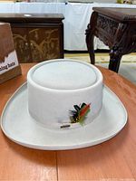 Front view of light gray Resistol beaver western hat with feathers on hatband on round wooden table.