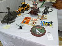 View of vintage toy helicopters, yellow CAT tractor, carousel model, Dennis the Menace books, Hot Wheels Rescue Duty toy car, and a diorama with a dog and pond