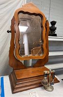 Front view of a vintage wooden vanity mirror with scalloped edges and dark trim, mounted on a wooden adjustable frame with a sturdy tiered base.