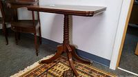 Side angle of vintage wood table showing rectangular top and turned pedestal base with four legs ending in brass claw feet on casters.