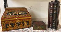 Photo showing 3 boxes including large lacquer box with boat figures, smaller red and gold box, and tri-book illusion storage box