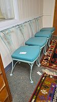 Four turquoise wrought iron chairs arranged in a row showing floral metalwork design and blue vinyl padded seats.