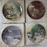 Four collector plates wrapped in plastic, showing various cottage scenes in color with some boxes with wear visible