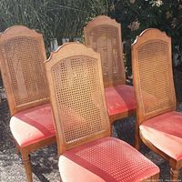 Four Drexel mid-century tall back chairs with cane backs and coral upholstered seats shown outdoors with sunlight highlighting wood grain and seat wear.
