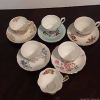 Photo showing entire set of six English china teacups and saucers with floral patterns and gold trim.