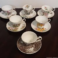 Front view of 6 English vintage tea cup and saucer sets arranged in 2 rows on a dark surface, each with different floral and scenic patterns