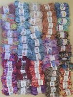 Multiple skeins of 50 gram yarn balls arranged side by side showing different colors and textures including blue, purple, brown, green, and multicolored yarns.