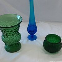 Three colored glass pieces: a tall blue swung vase, a large green crinkle vase, and a small emerald green fish scale pot.