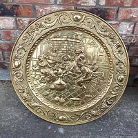 25 inch brass plate with an embossed scene showing four people sitting around a table inside a tavern setting, surrounded by decorative border.