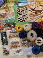 Photo showing two hemp jewelry books along with various hemp cords and multiple wooden beads in different sizes and colors organized on a surface.