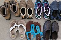 Front view of all seven pairs of shoes and sandals arranged on the floor showing various styles and colors including hiking boots, sneakers, sandals, and slip-on shoes.