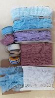 Top view of multiple lace trims in various colors and widths rolled or folded