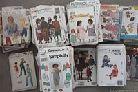 Photo showing assorted sewing patterns by McCall's, Butterick, Simplicity, Kwik Sew, and others featuring children's clothing and size ranges. Various cut and uncut patterns arranged side-by-side.