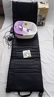 Full setup of the black Conair massage mat laid flat, white and purple Dr Scholl's foot spa bath with cord, and Obus Forme body massager in its original box, all displayed on a white background.