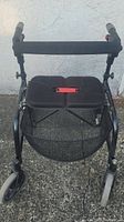 Front view of black Nexus 3 rollator walker, showing padded seat, mesh storage basket below, and part of the frame with decals.