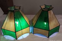 Photo showing the front and side of two hexagonal slag glass lampshades with alternating green and off-white panels.