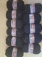 11 skeins of black Patons Classic Wool Tweeds yarn with colorful flecks, stacked in two columns.