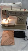 Singer Merritt sewing machine model 8374 with attached foot pedal and original instruction manual displayed beneath machine, beige protective cover in background.