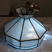 Front and side view of the 8-sided slag glass ceiling lamp illuminated, showing the opaque white slag glass panels with metal framing and brass ceiling mount