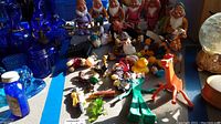 Photo showing ceramic 7 Dwarves figurines grouped together with various other collectible toys including characters like Tigger, Sylvester, and Tweety Bird on a table with a blue backdrop.