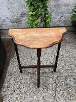 Front angle view of the antique wooden side table showing the scalloped top and turned legs with crossbars.
