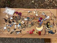 Overhead view of a diverse collection of costume jewelry including earrings and necklaces laid on a wooden surface with varied colors and designs.