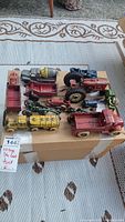 Entire lot of vintage die cast metal trucks and tractors shown on cardboard box with wear and partial paint loss.