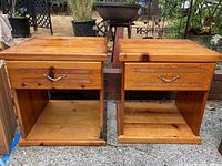 Pair of medium-tone wooden end tables photographed outdoors on a concrete surface. Left table shows drawer damage; both tables show usage marks.