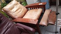 Wood framed reclining chair with light brown/tan leather cushions, extended footrest showing wear and color loss on leather.