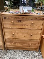 Full front view of the natural wood dresser showing all four drawers closed and round wooden knobs. The top surface has some minor items but contents not included in sale.