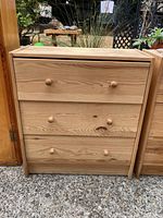 Front view of natural finish wooden dresser with three drawers and wood knobs, showing the overall design and condition.