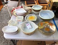 Photo showing various vintage Pyrex and ceramic cookware pieces and gravy boats arranged on a table, including bowls, casserole dishes and lids.