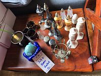 Full lot showing all salt and pepper shakers and metal napkin rings on wooden surface.