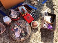 Wide view of multiple sewing supplies including scissors, buttons in containers, pincushion, tins and boxes of sewing accessories on a concrete surface.