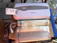 Top view of Rival Seal-a-Meal vacuum sealer with sealed FoodSaver vacuum sealing rolls and circular accessory in front.