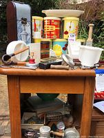 Wide view of multiple vintage kitchen items on a wooden table including colorful metal storage tins with fruit motifs and multiple kitchen utensils