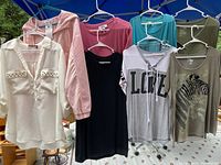 Photo showing seven hanging women's clothing items including various tops and jackets in multiple colors and styles.