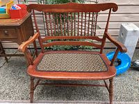Front view of wooden entryway bench showing floral upholstered seat, carved backrest, and armrests.