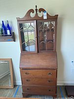 Full frontal view of the antique wooden secretary desk showing glass doors, curved top, and drawers below.
