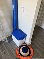 Photo showing Coleman cooler with blue lid, blue beach umbrella in carrying bag, and women's beach hats arranged nearby on the floor