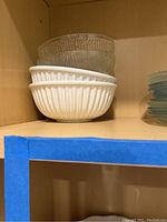 Four clear textured glass salad plates stacked on the right side, two white ribbed ceramic bowls stacked below two clear glass bowls on the left side in a wooden shelf.