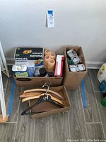 Boxes containing Philips light bulbs, painters rollers, spray paint, and denatured alcohol with boxes of assorted hangers in front.