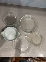 Top view of five dishes on countertop showing four clear glass round Pyrex ovenware dishes and one green floral patterned Pyrex dish