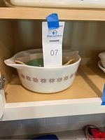 White vintage Pyrex handled casserole dish with brown decorative pattern on wooden shelf with blue tape.