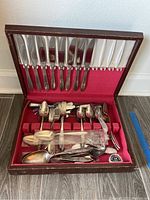 Opened wooden flatware chest showing silver knives, forks, spoons arranged inside with red fabric lining