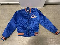 Full view of blue vintage Chalk Line NFL Denver Broncos jacket laid flat on floor showing front with snap buttons closed.
